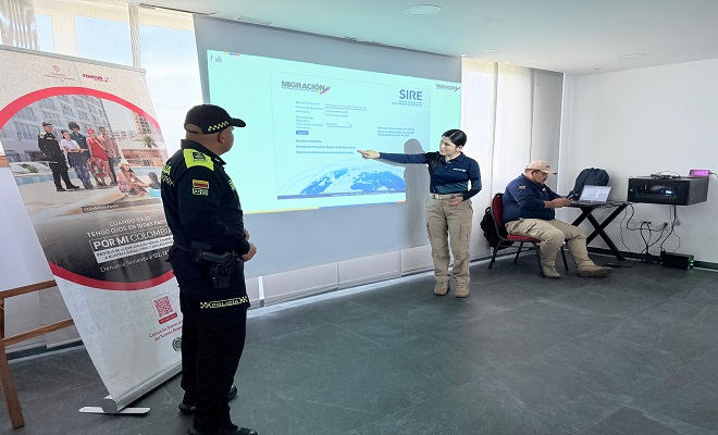 Uniformado del grupo de Turismo de la Polic&iacute;a Nacional en compa&ntilde;&iacute;a de una funcionaria de Migraci&oacute;n Colombia socializando el sistema SIRE mediante una pantalla 