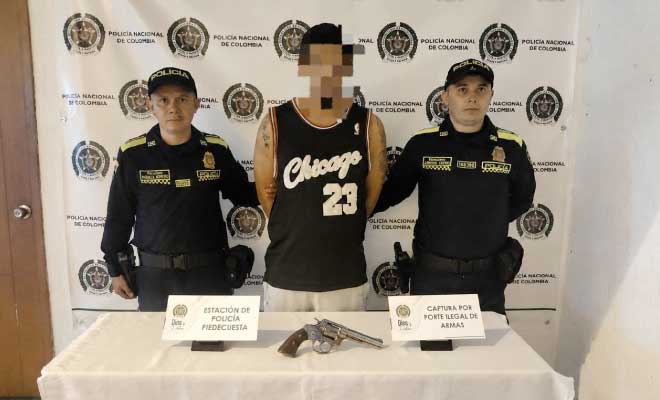 Hombre capturado en medio de dos Polic&iacute;as, en frente arma de fuego incautada