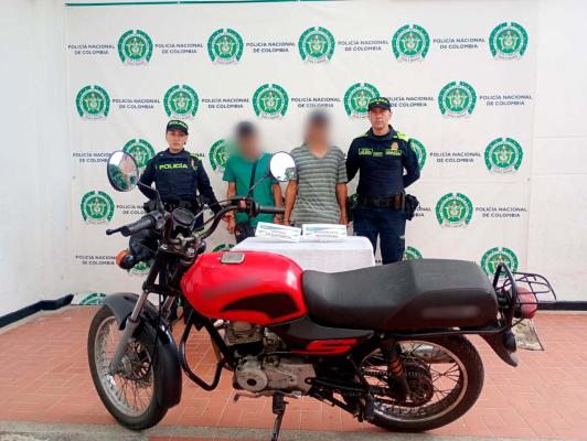 hombres capturados en medio de dos policias, en frente motocicleta recuperada